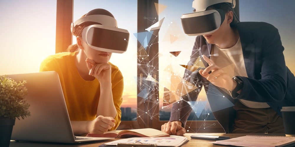 Due persone che indossano visori per la realtà virtuale, immerse in un ambiente digitale mentre collaborano su un progetto