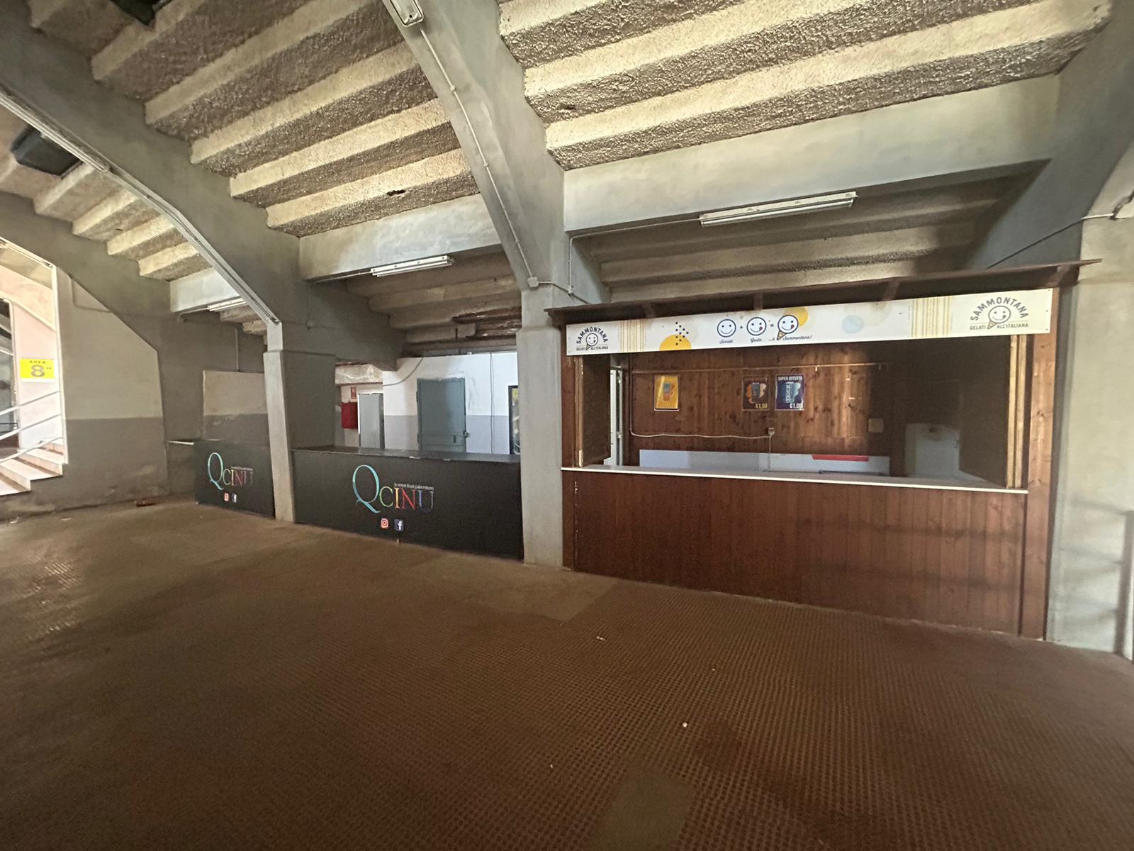 Vista degli spazi interni originali dello stadio Renzo Barbera di Palermo, con un’area ristoro non ristrutturata, caratterizzata da un bancone in legno e strutture in cemento a vista.